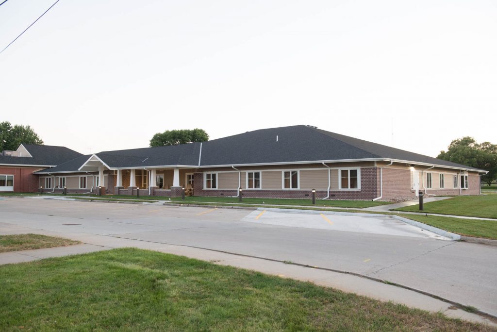 Corner view of single story, red brick and tan siding, health facility with white columns at entrance adjacent to a concrete parking lot