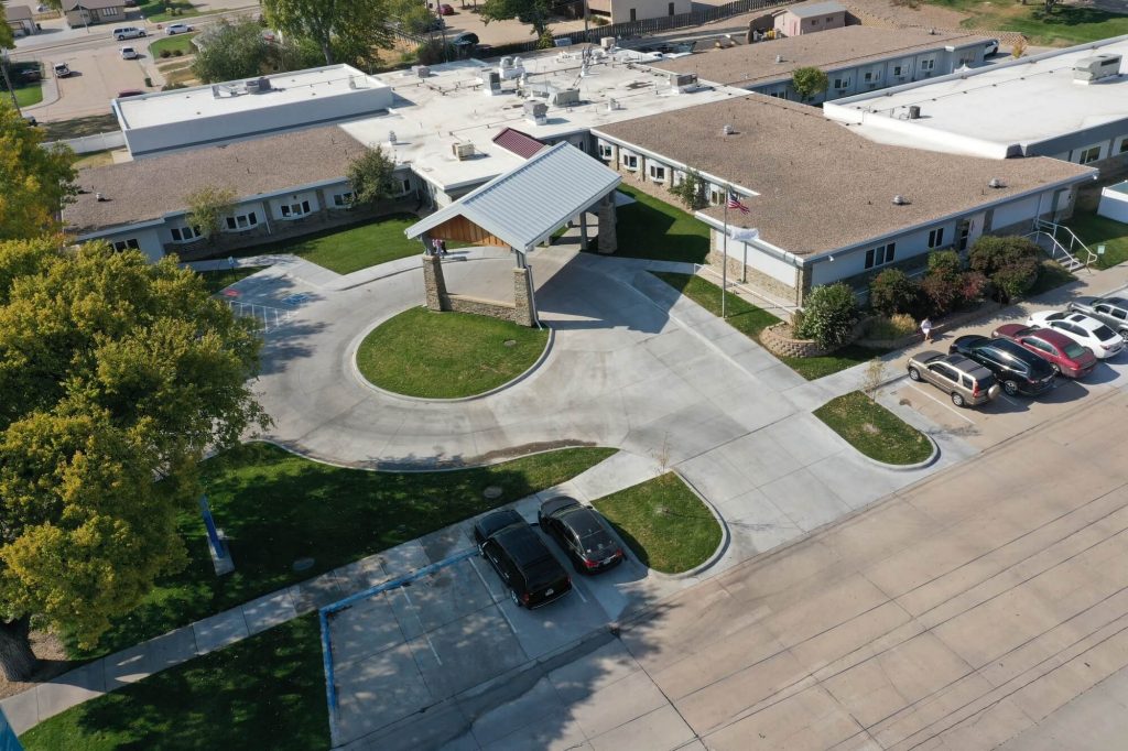 Arial corner view of a single story senior care facility with concrete roundabout at entrance partially covered by a metal structure
