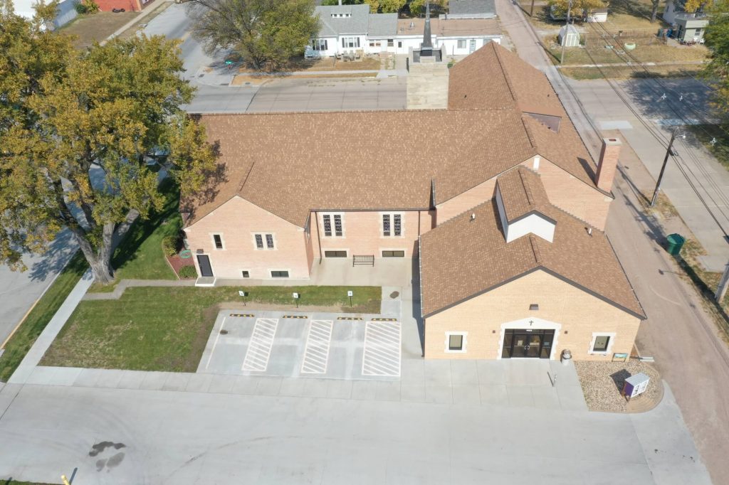 Clay colored brick, single story church adjacent to an established tree and a concrete parking lot