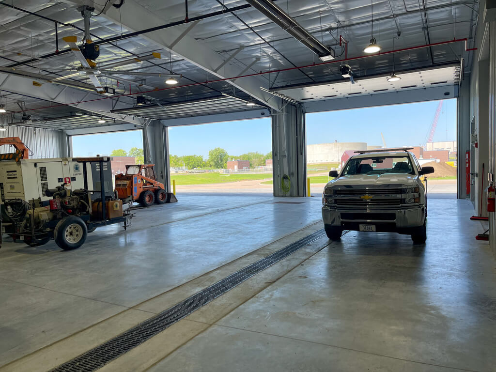 Inside an industrial building with metal walls and a white pickup truck, facing outward looking through the open garage doors